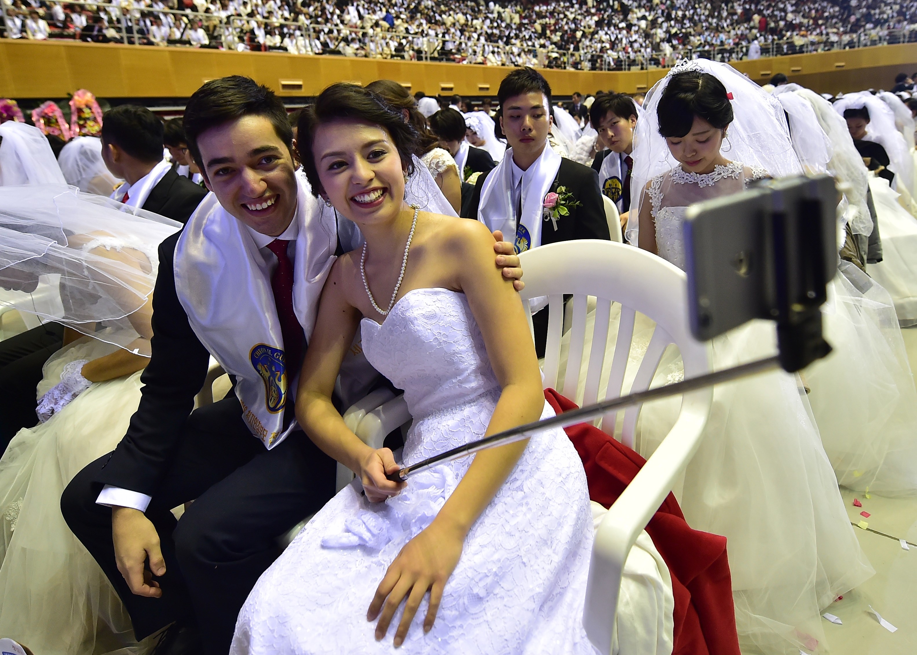 A couple take a selfie during a mass wedding held by the Unification Church at Cheongshim Peace World Center in Gapyeong, east of Seoul, on February 20, 2016. Hundreds of couples were married at the South Korean headquarters of the Unification Church. The Unification Church, set up by Sun Myung Moon in Seoul in 1954, is one of the world's most controversial religious organisations, and its devotees are often dubbed "Moonies" after the founder. AFP PHOTO / JUNG YEON-JE SKOREA--RELIGION-UNIFICATION-MARRIAGE